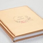 Detalle del grabado UV en un álbum de ecopiel dorada: nombre y adorno floral